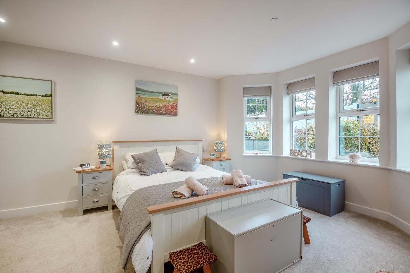 A bedroom with a bed, bedside tables, a bench, and a view of the outdoors through windows.