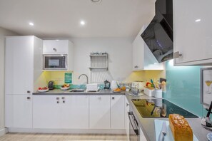 A modern kitchen with white cabinetry, a microwave, a sink, and a countertop with various kitchen items. - 2 Bed in Benllech (oc-t34071) (Benllech)