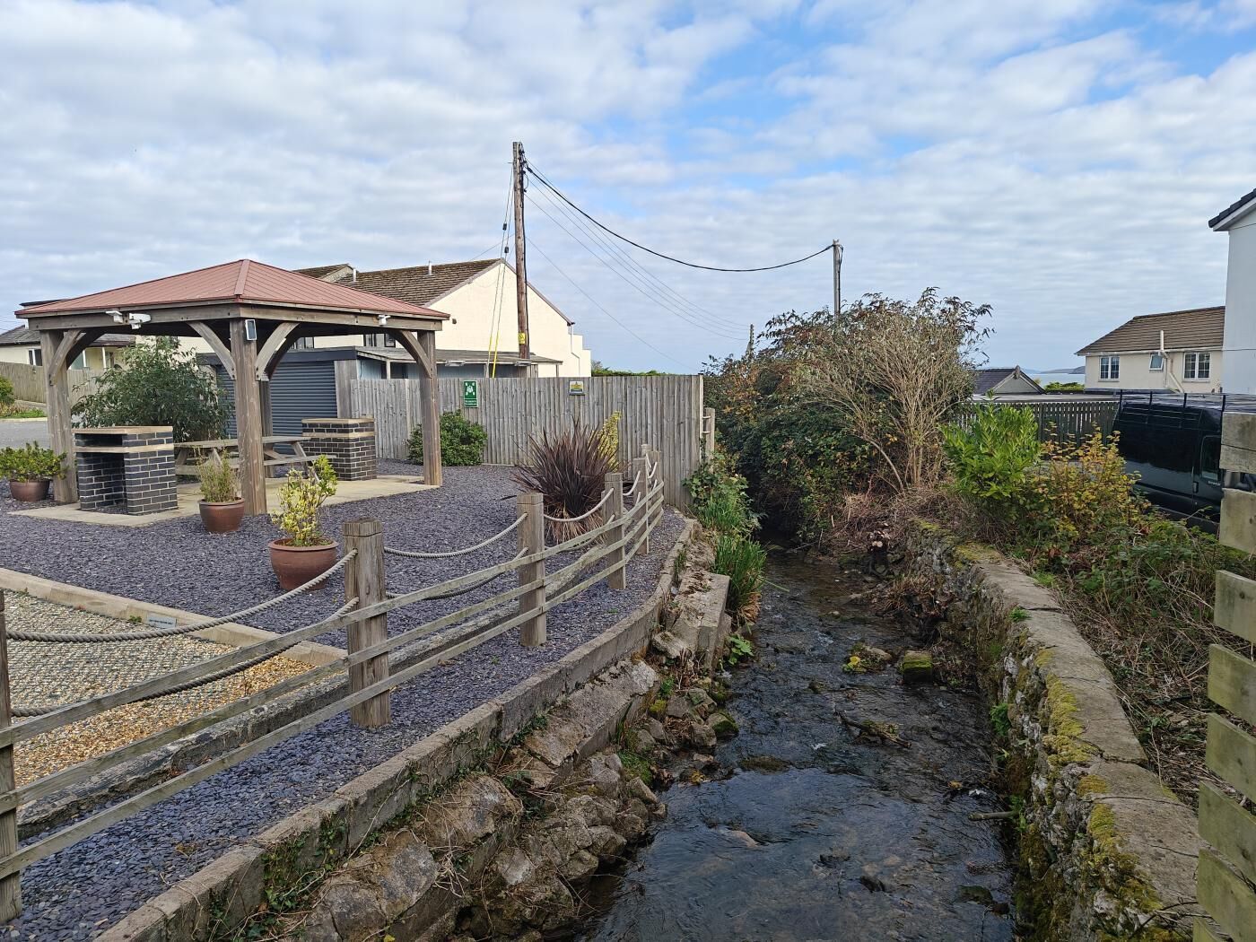 Un paseo ribereño con valla de madera, un pabellón y plantas en macetas.