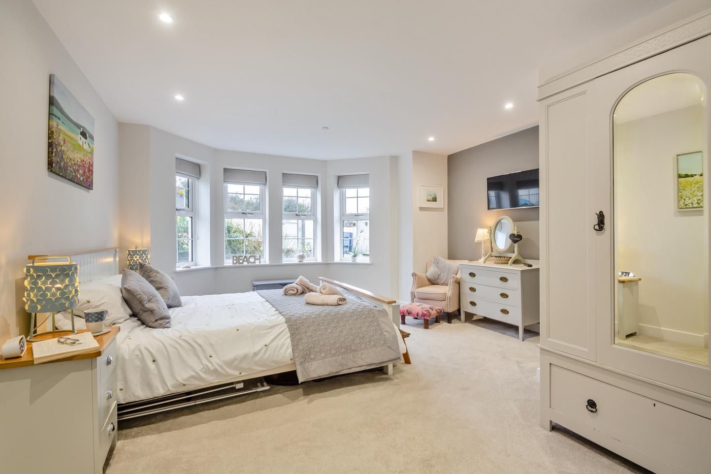 A bedroom with a bed, bedside tables, a dresser, a mirror, and large windows.