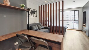 Uma sala de estar moderna com uma mesa de jantar de madeira, duas cadeiras, um sofá cinzento e uma estante decorativa com uma coruja de cerâmica e flores.
