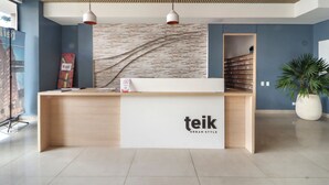 A reception desk with a "teik Urban Style" sign, a plant, and a wall with a textured pattern.