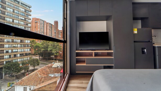 Quarto moderno com uma grande janela, televisão embutida e geladeira.