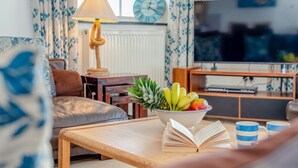 A cozy living room with a sofa, a coffee table with books and a bowl of fruit, a television, and a lamp. - 3 Bed in Polperro (oc-h34100) (Polperro)