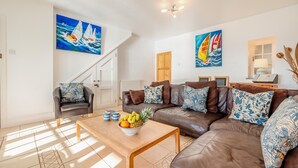 A living room with a brown leather sofa, a wooden coffee table with fruit, and two paintings of sailboats on the walls. - 3 Bed in Polperro (oc-h34100) (Polperro)