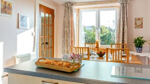 Eine gemütliche Küche mit Esstisch für zwei Personen, einem fenster mit Vorhängen und einer kleinen Pflanze auf der Fensterbank.