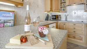 A kitchen with a bottle of wine, a glass, a cutting board with cheese and tomatoes, and a jar of jam. - 3 Bed in Lochearnhead (oc-c33641) (Lochearnhead)