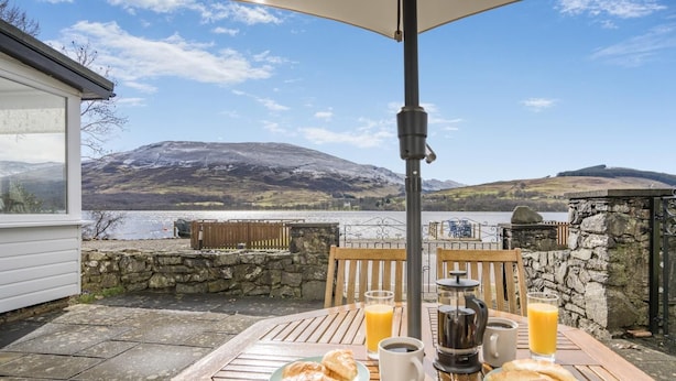 A table with breakfast items, a coffee maker, and a view of a lake and mountains. - 3 Bed in Lochearnhead (oc-c33641) (Lochearnhead)