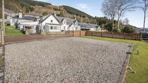 A residential area with houses, a gravel driveway, and a wooden fence. - 3 Bed in Lochearnhead (oc-c33641) (Lochearnhead)