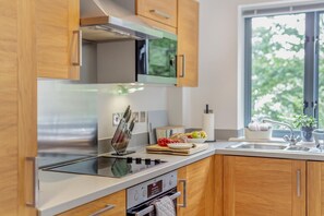 A modern kitchen with wooden cabinets, a stainless steel range, and a window providing a view of greenery outside. - 2 Bed in Fowey (oc-h33067) (Fowey)
