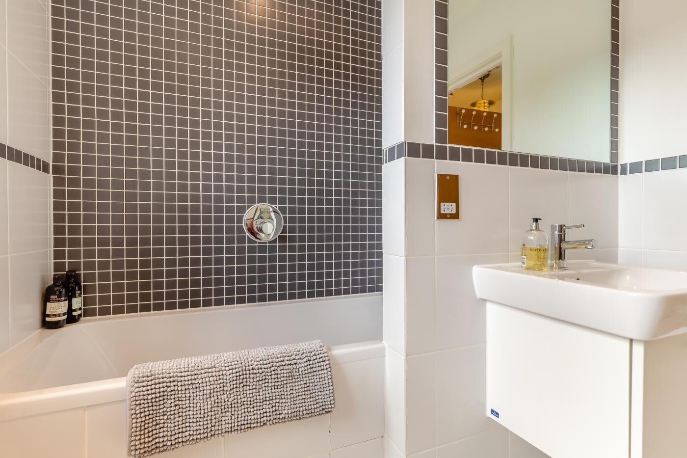 A bathroom with a tiled wall, a bathtub, a sink, and a towel.