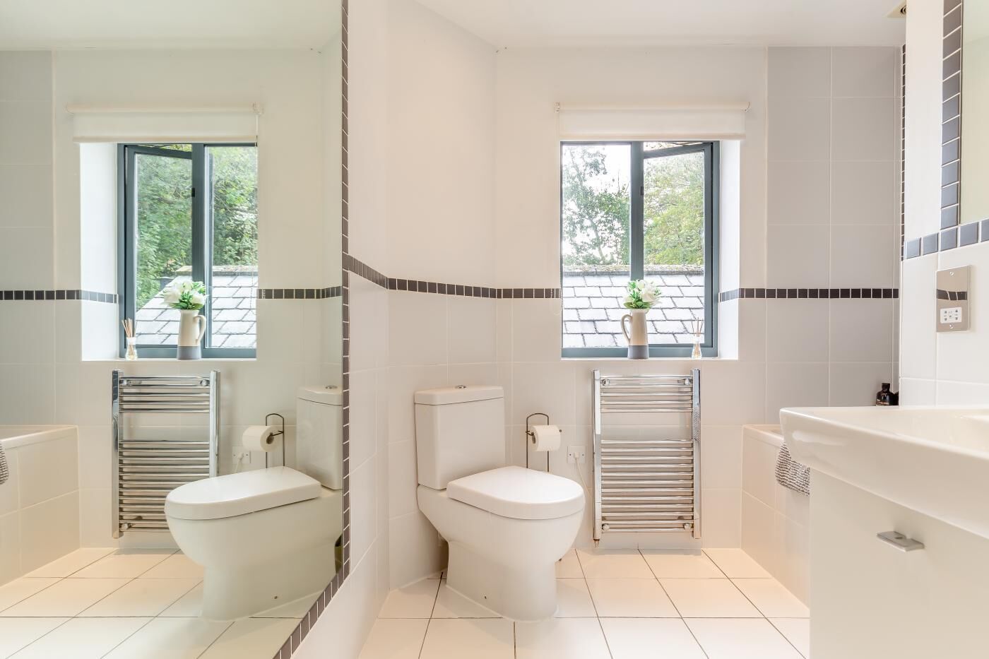 A modern bathroom with two toilets, a large mirror, and a window providing a view of greenery.
