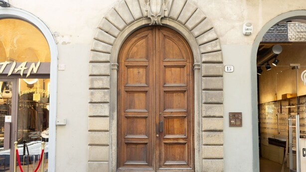 A double wooden door with a stone archway, a visible number plaque, and a glass entrance to a shop. - Vigna Nuova District Apartment (Firenze)