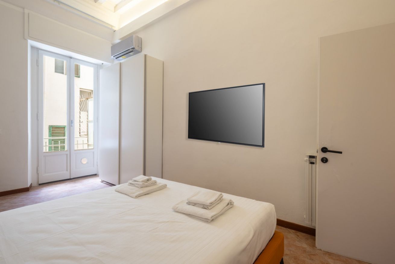 Een hotelkamer met een bed, een flatscreen televisie aan de muur en een deur naar een balkon.