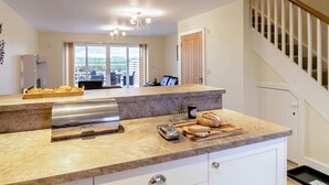 A modern kitchen with a marble countertop, a built-in oven, and a dining area with a table and chairs. - 2 Bed in Alnwick (oc-80497) (Newton-by-the-Sea)