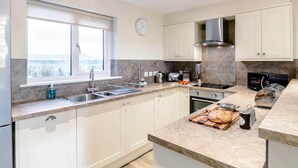 A modern kitchen with white cabinets, a large window, a built-in oven, and a countertop with bread and jars. - 2 Bed in Alnwick (oc-80497) (Newton-by-the-Sea)