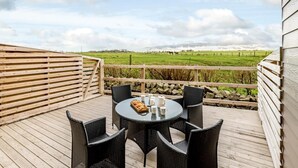 A wooden deck with a round table and chairs, overlooking a green field with horses. - 2 Bed in Alnwick (oc-80497) (Newton-by-the-Sea)