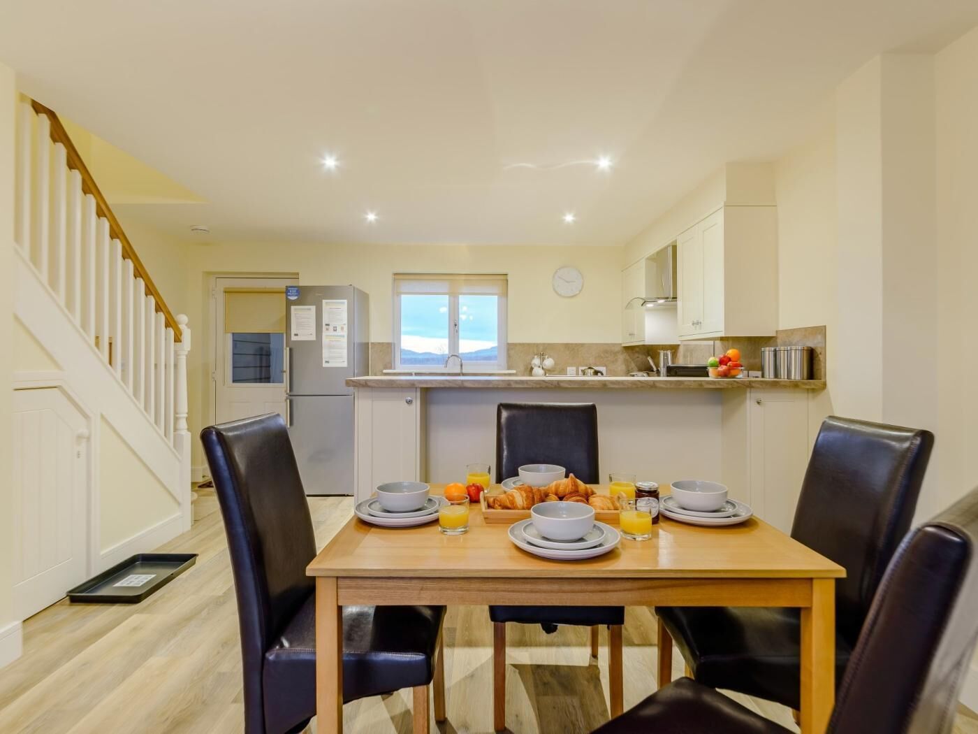 A dining area with a table set for breakfast, including croissants, orange juice, and bowls.