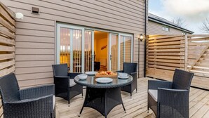 Une terrasse avec une table ronde et quatre chaises, une porte-fenêtre coulissante donnant sur une pièce intérieure et une terrasse en bois.