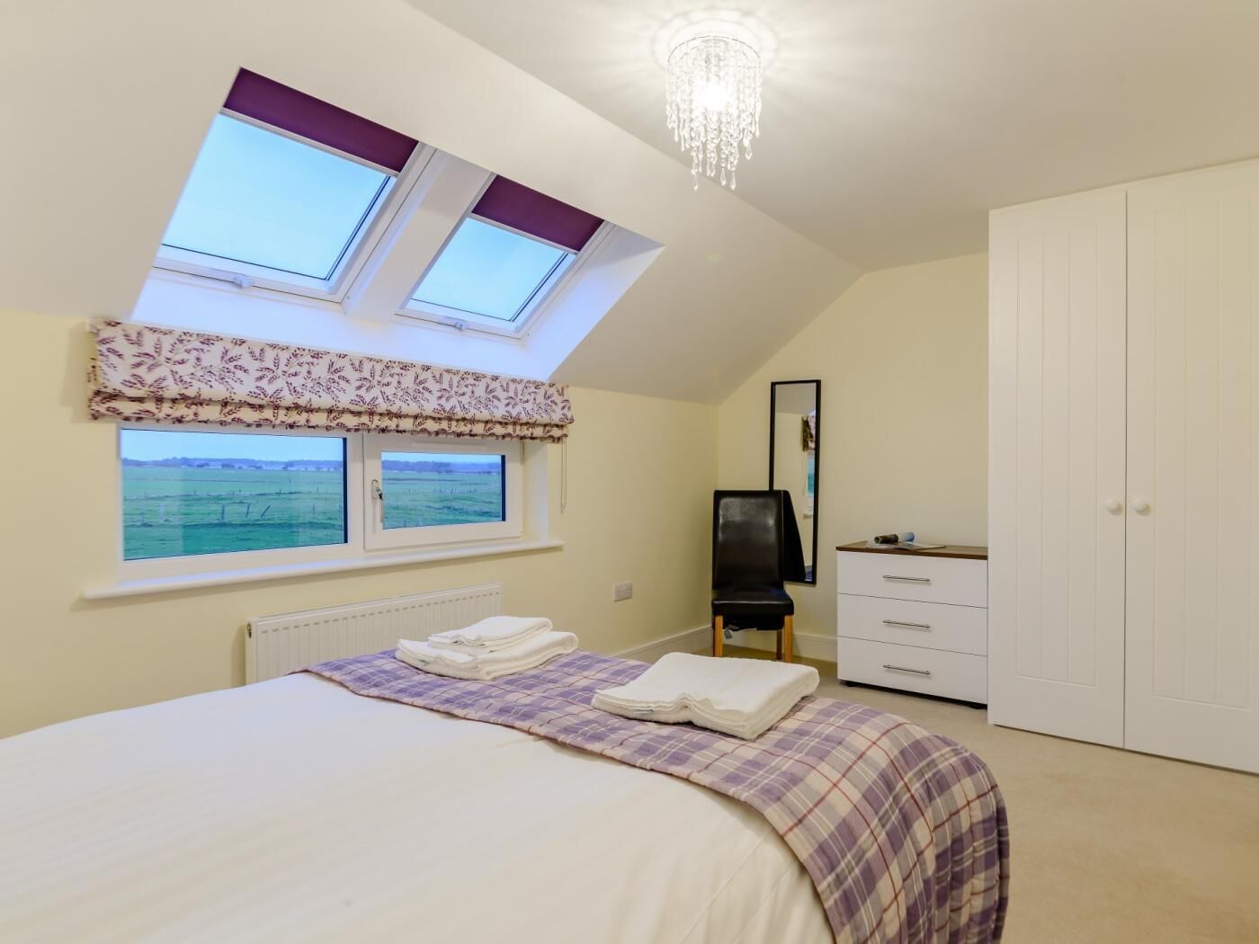Une chambre à coucher comprenant un lit, une commode, une chaise, un miroir et une vue sur la mer par une fenêtre.