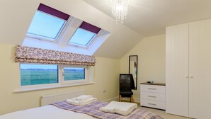 Une chambre à coucher comprenant un lit, une commode, une chaise, un miroir et une vue sur la mer par une fenêtre.
