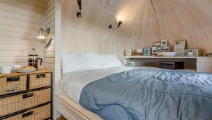 Une chambre confortable avec un lit, une table basse, des paniers en osier et des luminaires fixés au mur.