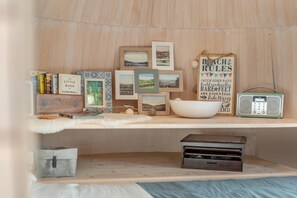 A cozy room with a wooden shelf displaying books, framed pictures, a bowl, a radio, and a small wooden box.