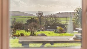 A view through a window of a rural landscape with a grassy field, a wooden bench, and a building in the distance. - 1 Bed in Widegates (oc-j34234) (Deviock)