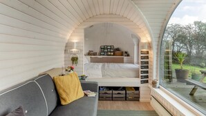 A cozy bedroom with a curved ceiling, a bed with a headboard, a bedside table with a lamp, and a view of the outdoors through a large window. - 1 Bed in Widegates (oc-j34234) (Deviock)