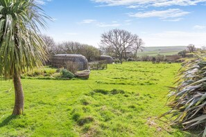 A rural landscape with green fields, a palm tree, and several hay bales.