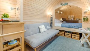 En ombonad inredning med en soffa, ett litet bord med en växt och en säng med en sänggavel i trä.