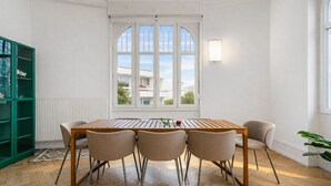 Zona pranzo con tavolo in legno e quattro sedie, un mobiletto verde e una finestra con vista sugli edifici.