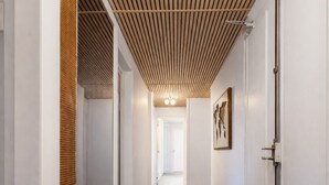 Un corridoio con soffitto a listelli di legno, pareti bianche e tappeto a motivi.