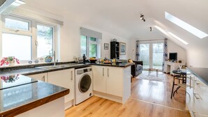 A modern kitchen with a washing machine, a dining area with a table and chairs, and a large window providing natural light. - 1 Bed in Hindhead (oc-w34256) (Haslemere)