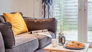 A cozy living room with a grey sofa, a yellow pillow, a coffee table with a croissant plate, a coffee pot, and a white mug. - 1 Bed in Hindhead (oc-w34256) (Haslemere)