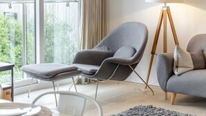 A modern living room with a grey armchair, a matching ottoman, a sofa, and a floor lamp. - 4 Bed in Widemouth Bay (oc-s34119) (Widemouth Bay)