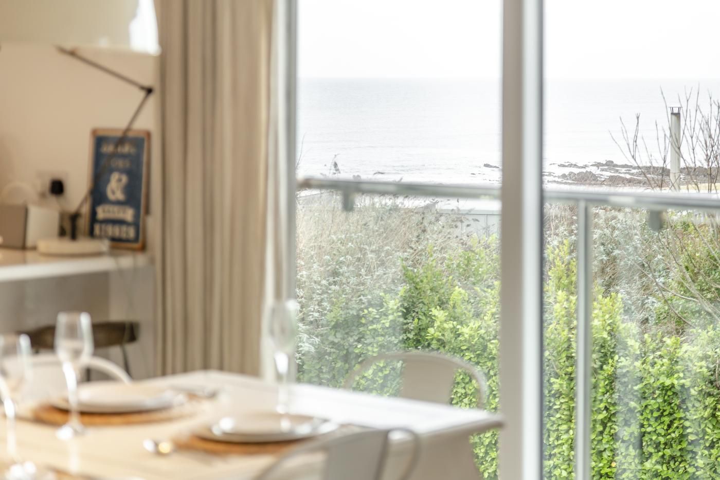 A dining area with a table set for two, a view of the sea, and a sign on the wall.