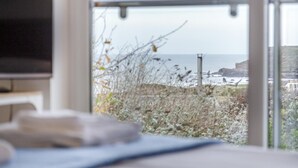 A room with a large window overlooking a coastal view, including a rocky shoreline and the sea. - 4 Bed in Widemouth Bay (oc-s34119) (Widemouth Bay)