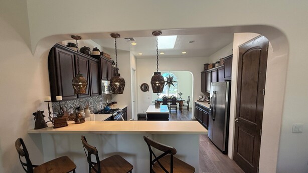 A modern kitchen with dark wood cabinets, a central island with bar stools, and a stainless steel refrigerator. - Luxury Vacation Rental in historic Tubac, Arizona --Come see Southern Arizona! (Tubac)