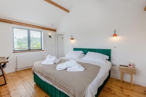 Een slaapkamer met een bed, een radiator, een raam met zonwering, een nachtkastje en een bedtafeltje met een lamp.