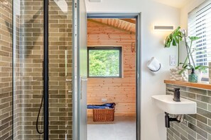 Een moderne badkamer met een douche, een wastafel en een raam met uitzicht op groen.