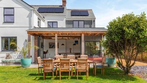 Une maison à deux étages dotée d’un patio couvert, de panneaux solaires et d’un jardin bien entretenu.