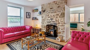 Un salon avec une cheminée en pierre, un canapé rose, un tapis à motifs zébrés et une bibliothèque.