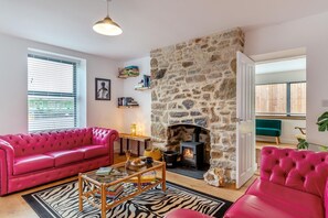 Een woonkamer met een stenen openhaard, een roze bank, een tapijt met zebraprint en een boekenkast.