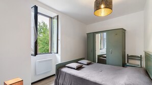 Un dormitorio con cama, armario, ventana y lámpara.