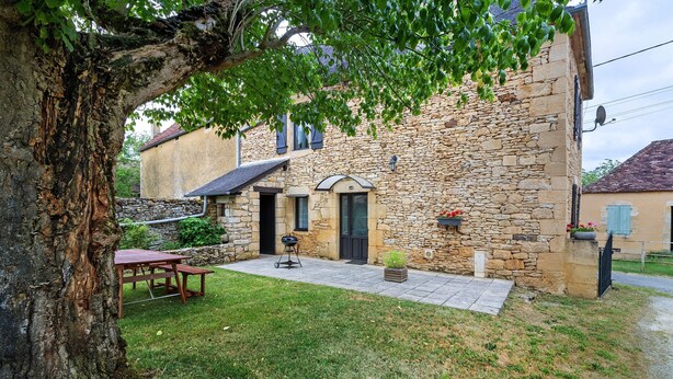 Un edificio de piedra con un patio, un árbol y una mesa.