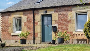 A traditional brick house with a blue door, two windows, and a small porch with a bench.