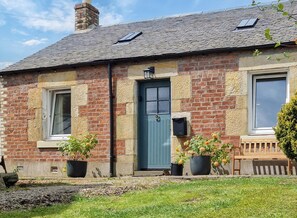 A traditional brick house with a blue door, two windows, and a small porch with a bench.