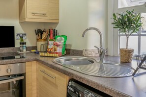 A modern kitchen with a stainless steel sink, wooden cabinets, and a dish rack with kitchen essentials. - 1 Bed in Errol (oc-s33022) (Errol)