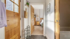 Un corridoio con porte in legno, un portaoggetti metallico, una piccola pianta e un letto in lontananza.